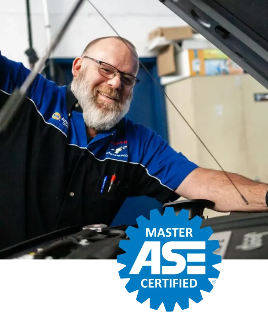 Smiling ASE Master Certified mechanic at Cain and Sons’ Automotive in Glen Rock, PA working under a raised car hood.