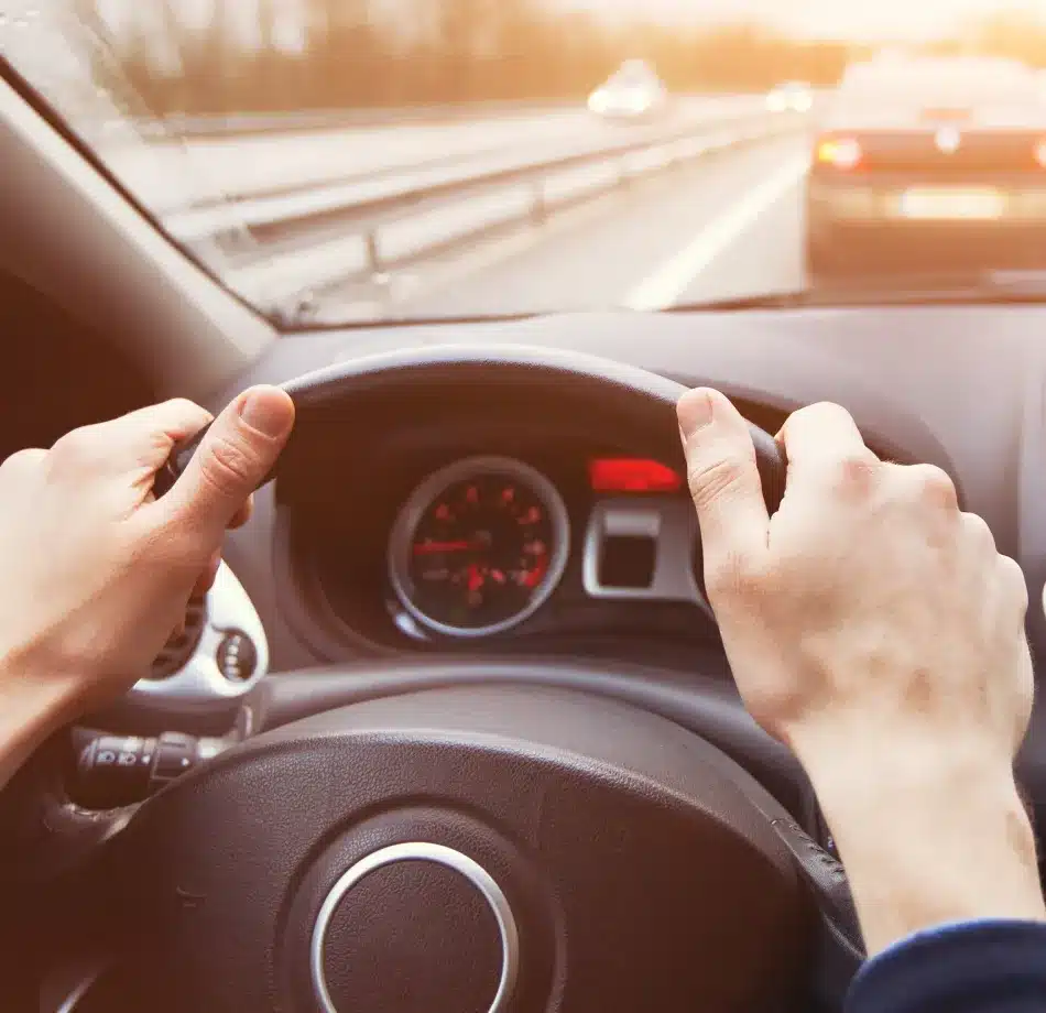 Driver’s hands on a steering wheel while traveling on the highway at sunset, representing safe and reliable auto repair with Cain and Sons in Glen Rock, PA.