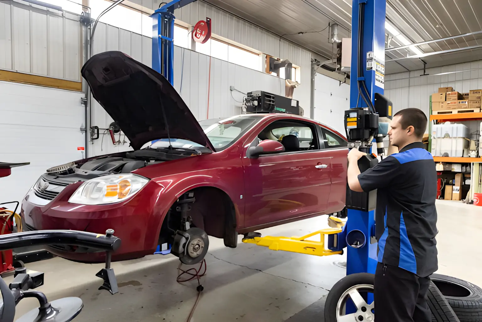 Back-to-school car maintenance in Glen Rock, PA by Cain and Son’s Automotive. Image showing a mechanic working on a maroon sedan lifted in the shop with the front wheels removed, emphasizing professional brake service and vehicle maintenance.