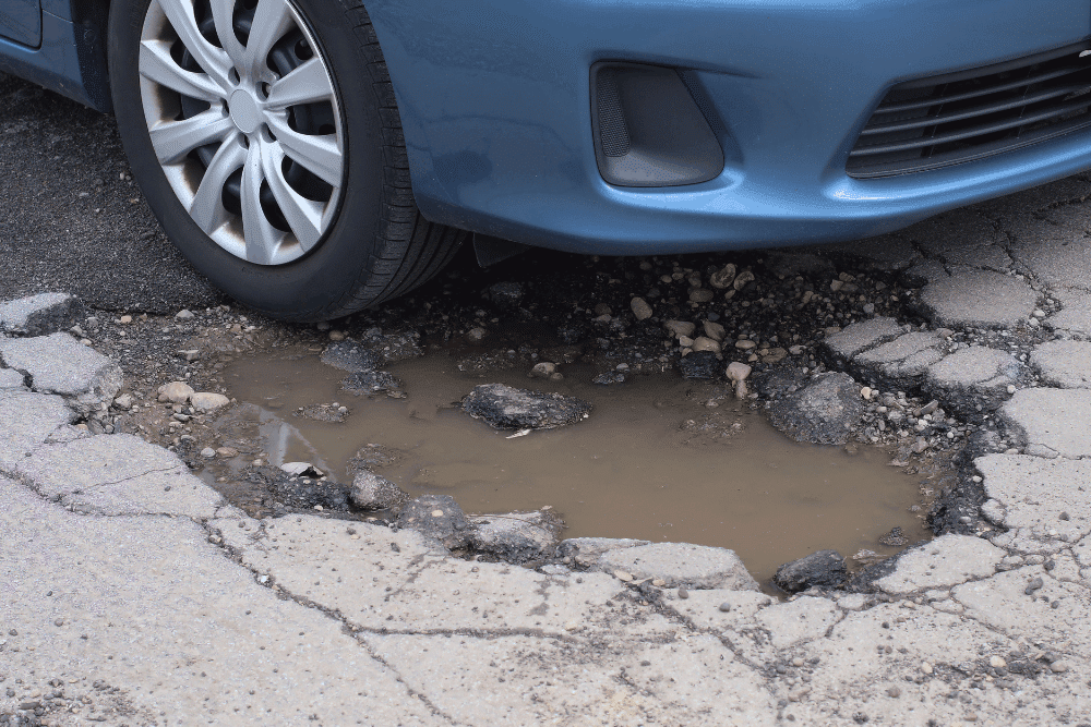Pothole damage, auto repair in Glen Rock, PA by Cain and Son’s Automotive. Image of a vehicle wheel sitting in a deep pothole, highlighting road damage that can cause misalignment, suspension wear, and tire issues.
